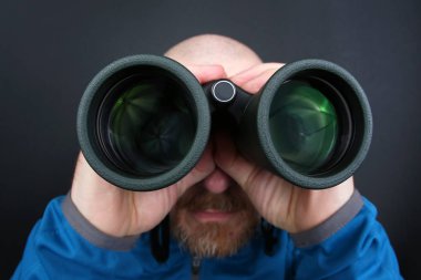 sakallı adam gri arka plan üzerinde dürbün üzerinden seyir