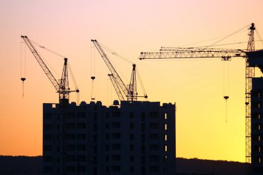 Günbatımı gökyüzünün arka planında inşa edilmiş evler olan vinçler.