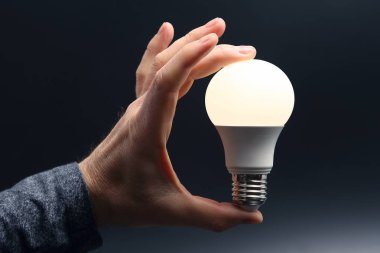 Koyu arka plan üzerinde insan elinde yeni LED lamba dahildir
