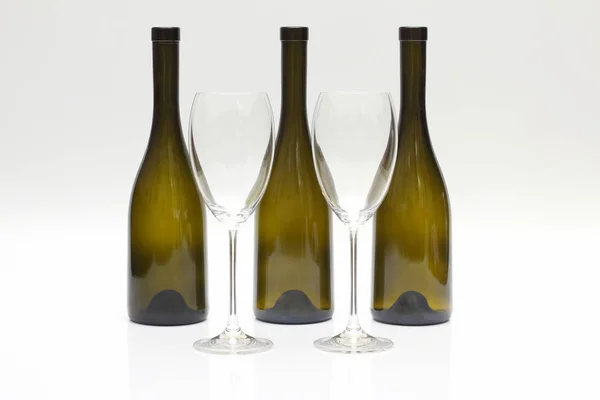 Tři prázdné otočené lahví vína a dvě skleničky na bílé bac — Stock fotografie
