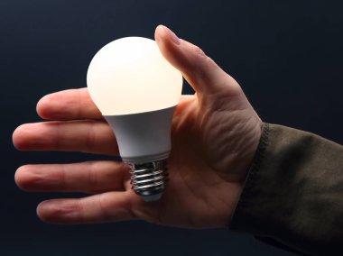 Koyu arka plan üzerinde insan elinde yeni LED lamba dahildir