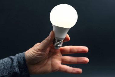 Koyu arka plan üzerinde insan elinde yeni LED lamba dahildir