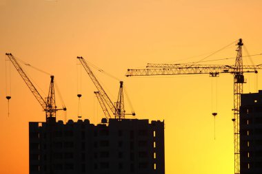Günbatımı gökyüzünün arka planında inşa edilmiş evler olan vinçler.