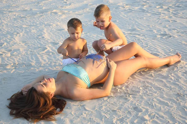 young children paint on the belly of a pregnant mother