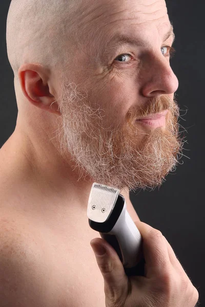 Skäggig man med trimmer för att justera skägg i handen — Stockfoto