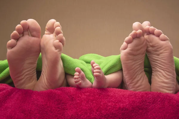 Feet of newborn baby and parents together on the bed — Stock Photo, Image