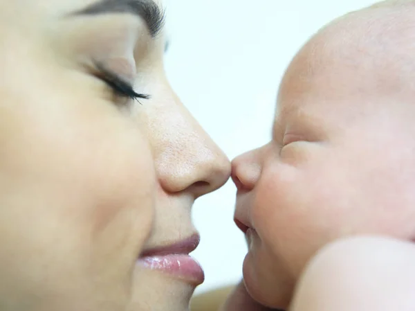 mom touches her nose on the nose of a sleeping newborn baby clos