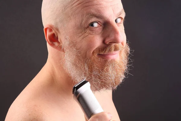Bearded man with trimmer to adjust beard in hand