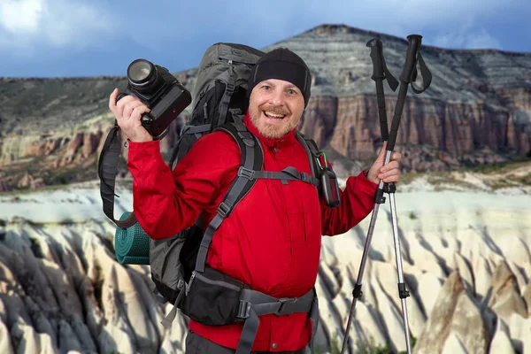 Happy traveler with a camera and trekking poles in his hands on Stock Picture