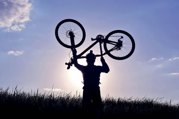 一个骑自行车的人的剪影与一个凸起的自行车在草地上 — 图库照片