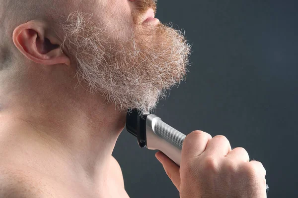 Bearded man with trimmer to adjust beard in hand
