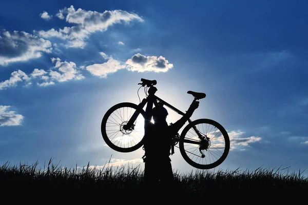 Silhouette eines Radfahrers mit einem hochgezogenen Fahrrad im Gras in der s — Stockfoto