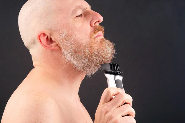 Homem barbudo com aparador para ajustar a barba na mão — Fotografia de Stock