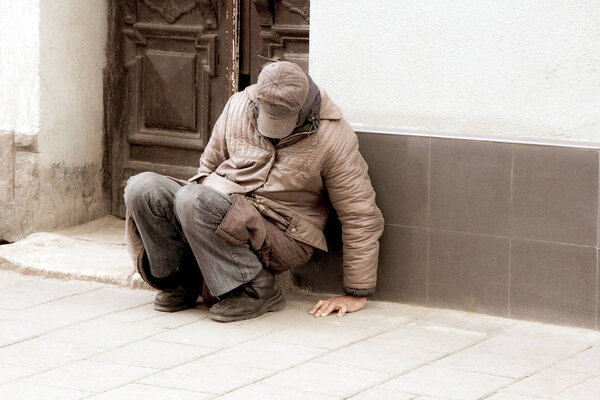 poor homeless man sitting near the wall of the building