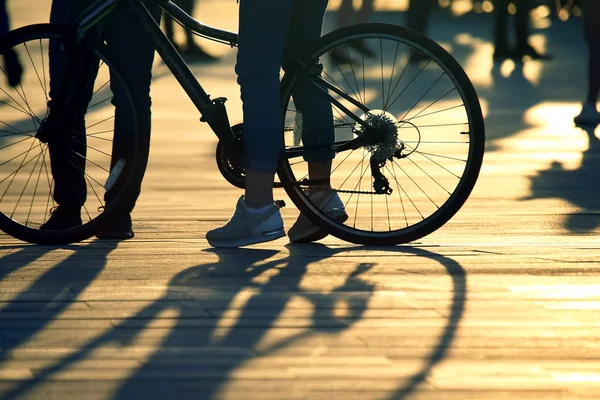 Pieds avec vélo et personnes derrière le soleil couchant — Photo