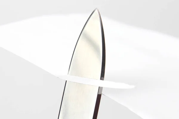 Lâmina de uma faca afiada cortada através do papel branco — Fotografia de Stock