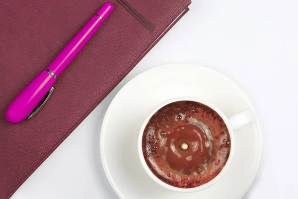 La penna rossa è sulla tazza con caffè nero e un notebook — Foto Stock