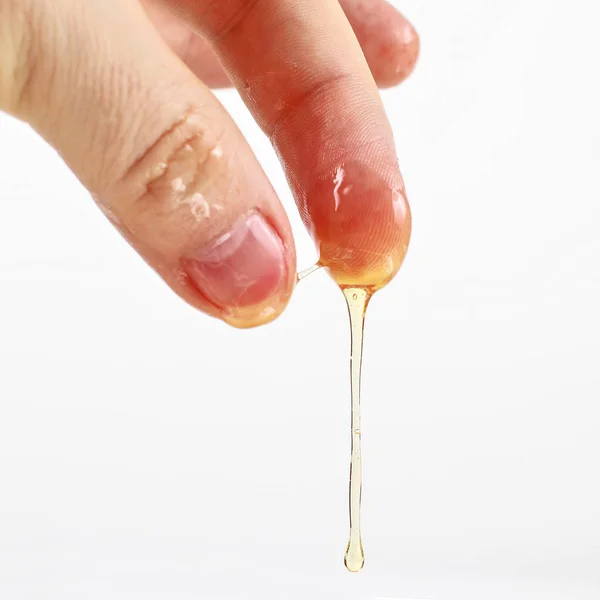 Miele scorre dalle dita su sfondo bianco — Foto Stock