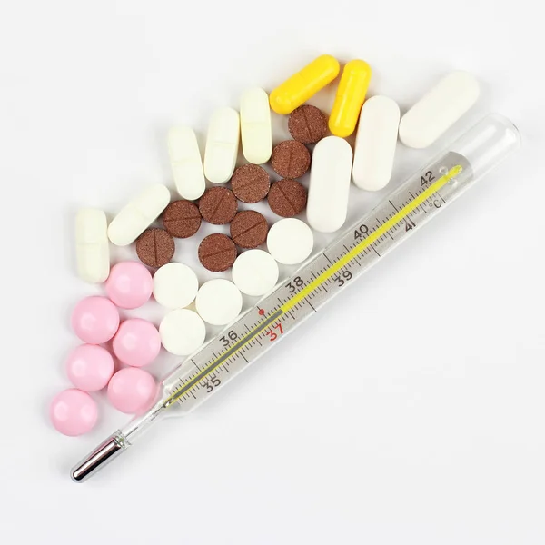 Thermometer und medizinische Pillen auf weißem Hintergrund — Stockfoto