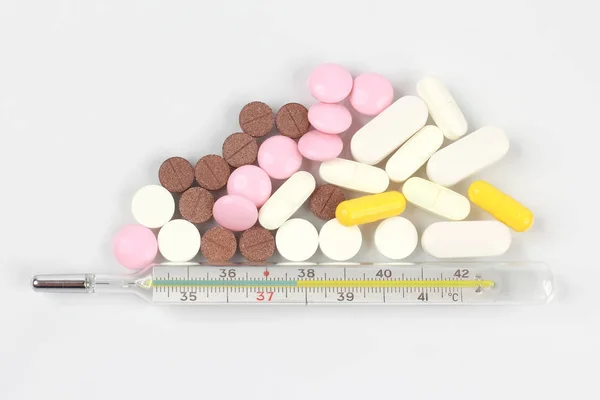 Лекарственные таблетки, термометр на белом фоне — стоковое фото