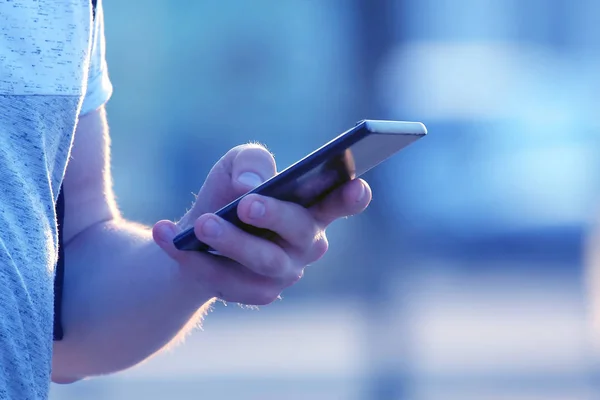 The hand of a man with a mobile phone on the street