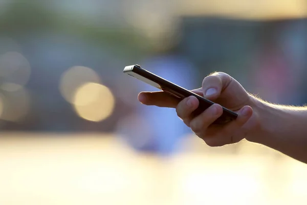 The hand of a man with a mobile phone on the street.