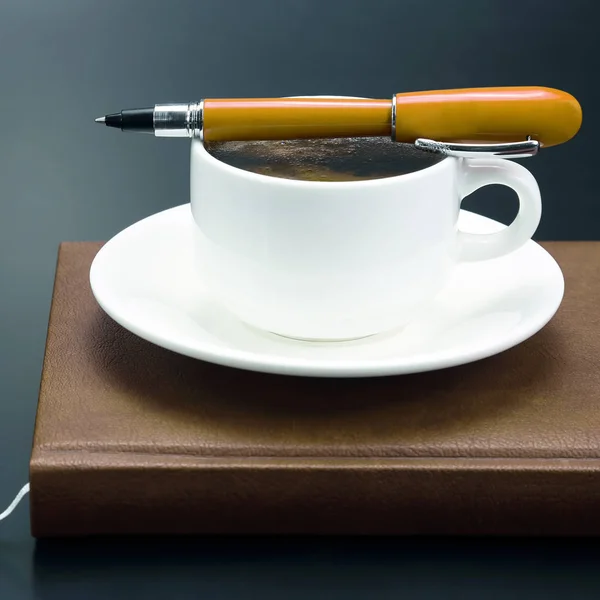 Penna rossa è sulla tazza con caffè nero e un noteboo — Foto Stock