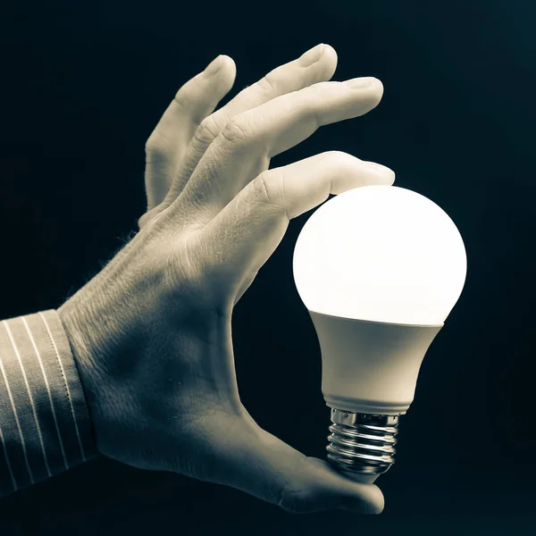 Mano umana che tiene la lampada a led inclusa su uno sfondo scuro . — Foto Stock