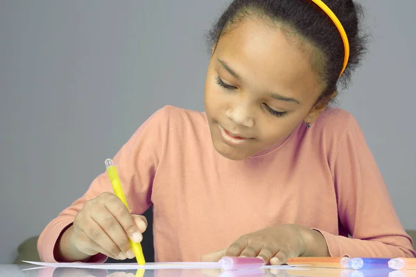 The girl draws a yellow pencil on white paper — Stock Photo, Image