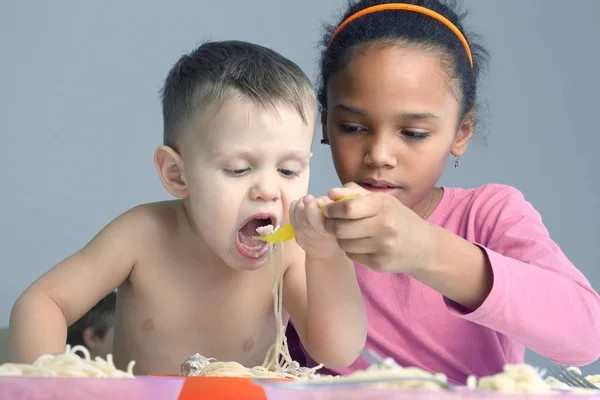 La ragazza aiuta il bambino a mangiare spaghetti — Foto Stock