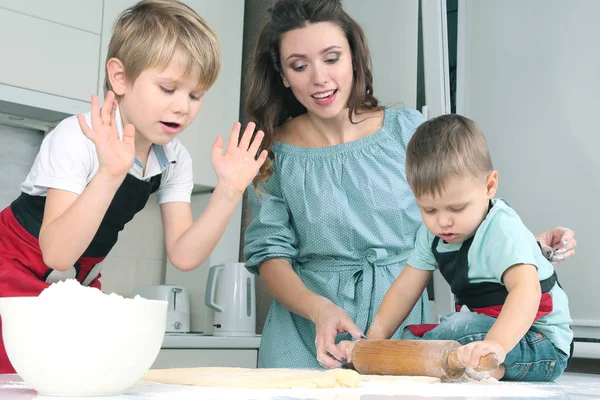 mom helps young sons knead the dough on the kitchen tabl