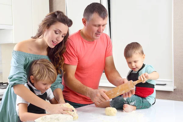 young parents help young sons knead the dough on the kitchen tab