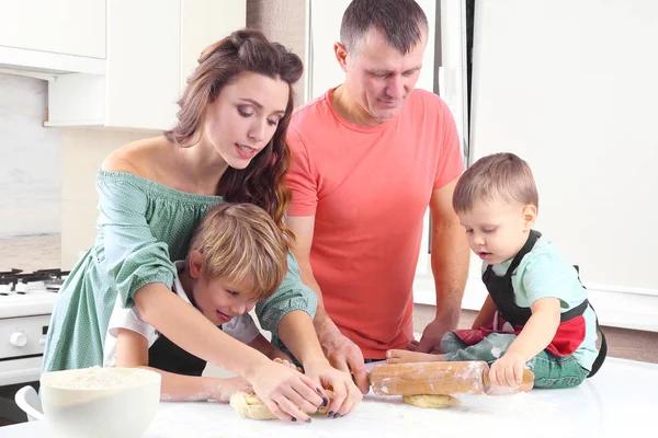 young parents help young sons knead the dough on the kitchen tab