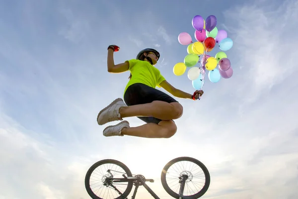 Meisje fietser springt in de lucht met ballonnen op fiets achtergrond — Stockfoto