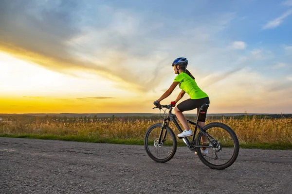 Schöne Radfahrerin, die mit dem Fahrrad auf der Straße in Richtung Sonne fährt — Stockfoto