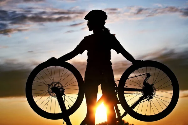 Silhouet van een meisje fietser met een fiets in zijn handen tegen — Stockfoto