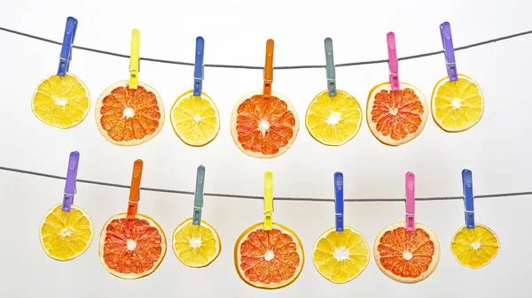 Many dried pieces of different citrus fruits hang on colored clo