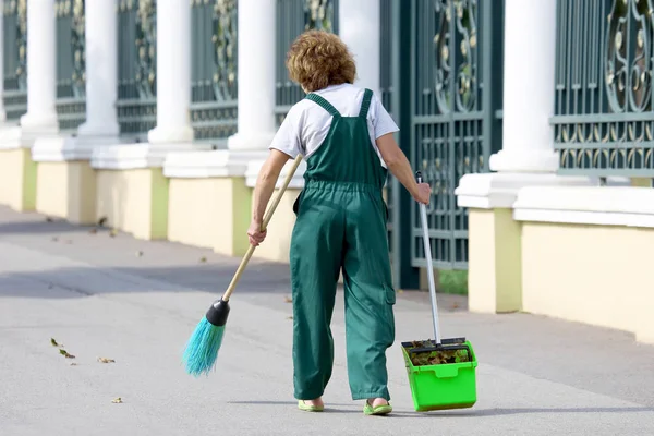 janitor cleans the sidewalk of the city from fallen leaves
