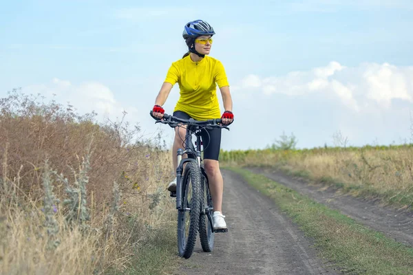 Schöne Radfahrerin fährt auf dem Feld auf dem Fahrrad. — Stockfoto