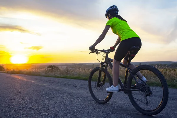 Schöne Radfahrerin fährt Fahrrad auf der Straße in den Sonnenuntergang — Stockfoto