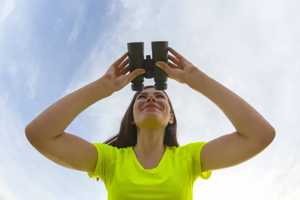 Ragazza in giacca gialla guardando attraverso binocoli contro la s — Foto Stock