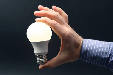 İnsan eli, içinde kurşun lambayı koyu bir arka planda tutuyor. elektrik ve LED endüstrisi