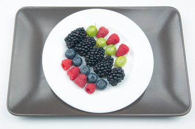 Beyaz tabakta böğürtlen, yabanmersini, bektaşi üzümü ve böğürtlen. Sağlıklı meyve vitamini. sağlıklı sebze kahvaltısı