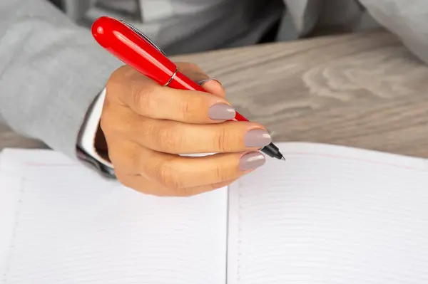 一个女商人的手拿着一支红笔放在笔记本的背面 — 图库照片