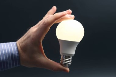 İnsan eli, içinde kurşun lambayı koyu bir arka planda tutuyor. elektrik ve LED endüstrisi