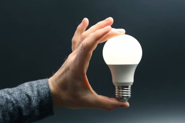 İnsan eli, içinde kurşun lambayı koyu bir arka planda tutuyor. elektrik ve LED endüstrisi