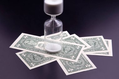 Dolar banknotları kum saatinin yanında. Vakit nakittir. Maaş. Zamanla iş çözümleri. Kum saati ölçümü