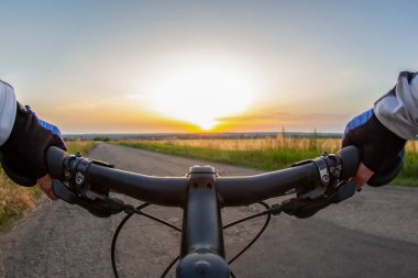 Eldivenli bisikletçi gün batımının güneşli gökyüzüne doğru yol boyunca gidiyor. Spor ve seyahat.