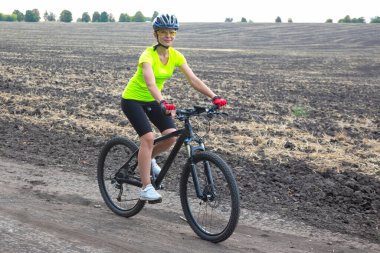 Güzel bir bisikletçi kız sahada bisiklet sürüyor. Sağlıklı yaşam tarzı ve spor. Boş zaman ve hobiler.