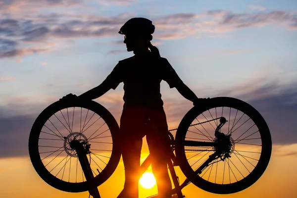 日没の空を背景に自転車で自転車を持つ少女サイクリストのシルエット 健康的なライフスタイルとスポーツ — ストック写真